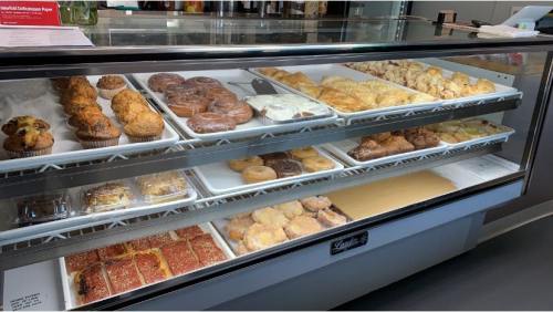 A display case filled with various baked goods, including muffins, donuts, pastries, and cookies.