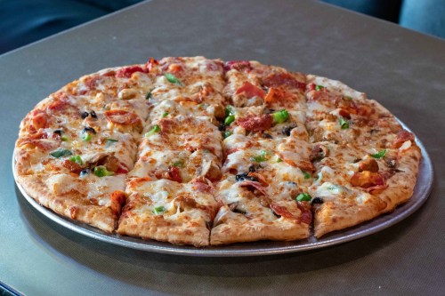 A large, round pizza topped with cheese, pepperoni, green peppers, and olives, sliced into equal pieces.