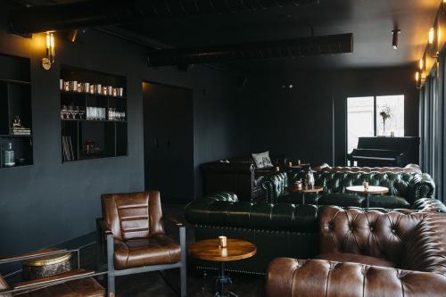 A stylish lounge with dark walls, leather sofas, wooden tables, and soft lighting, creating a cozy atmosphere.