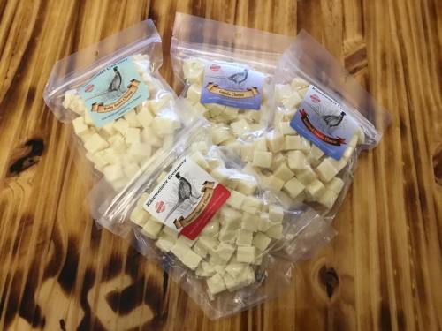 Four bags of cubed cheese on a wooden surface, each labeled with different flavors.