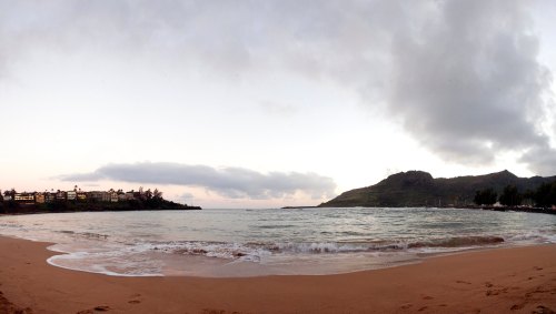 A serene beach scene at sunset, with gentle waves, distant hills, and a cloudy sky.