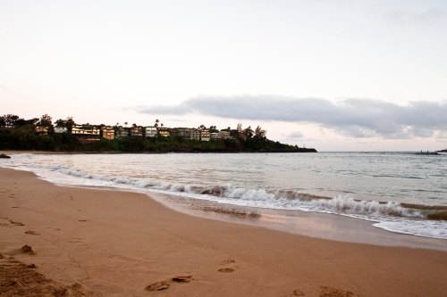 A serene beach scene at dusk, with gentle waves lapping at the shore and a distant resort along the coastline.