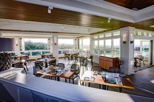 Bright, modern restaurant interior with wooden tables, chairs, and large windows showcasing a scenic view.