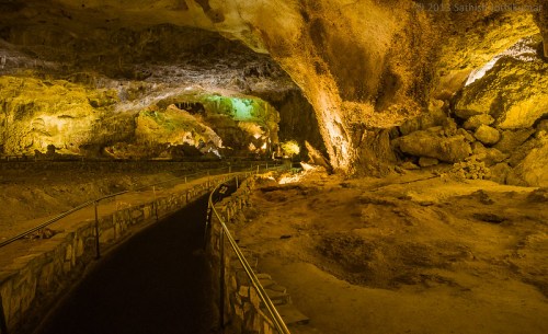 A dimly lit cave interior with rocky formations and a winding path, illuminated by soft green and yellow lights.