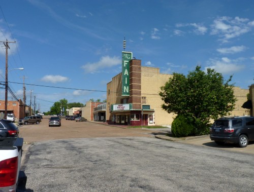 A vintage theater building with a marquee, surrounded by a quiet street and blue sky with scattered clouds.