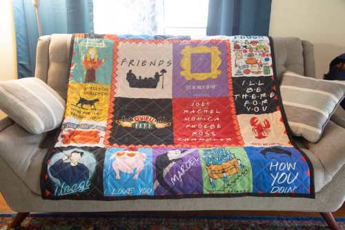 A colorful quilt featuring iconic quotes and images from the TV show "Friends," draped over a couch.
