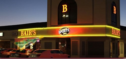 A brightly lit sports grill named "Bair's" at dusk, with neon signage and parked cars in front.