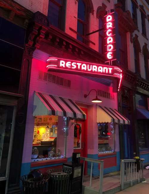 A brightly lit restaurant with a retro neon sign reading "Arcade Restaurant," featuring colorful window displays.