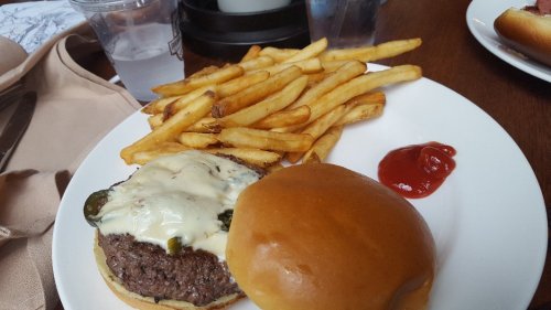 A plate with a cheeseburger topped with jalapeños, golden fries, and a side of ketchup.