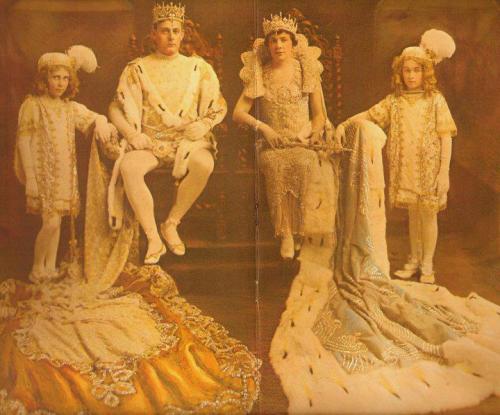A royal family in ornate costumes, seated on a throne, with two children and two adults, adorned with crowns and elaborate gowns.