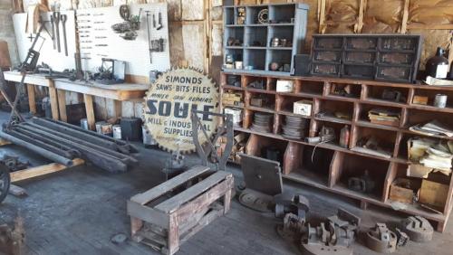 A vintage workshop filled with tools, shelves, and a sign for industrial supplies, showcasing a rustic, organized space.
