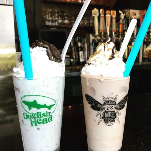 Two milkshakes in tall glasses, one topped with whipped cream and an Oreo, the other with chocolate drizzle and a straw.