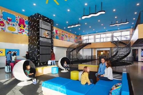Bright, modern lobby with colorful decor, seating areas, and a spiral staircase; families and children are enjoying the space.