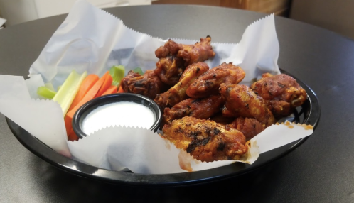 A black platter with crispy chicken wings, celery, carrot sticks, and a small bowl of ranch dressing.