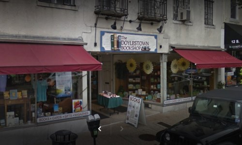 A quaint bookshop with large windows, colorful signage, and outdoor displays of books and gifts.