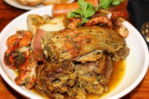 A bowl of seafood and meat, featuring shrimp, seasoned crab, and potatoes, garnished with parsley.