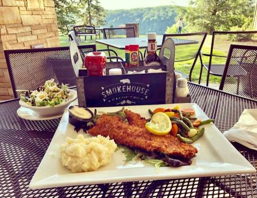 A plate of fried fish with lemon, mashed potatoes, mixed vegetables, and a side salad, set on a table outdoors.