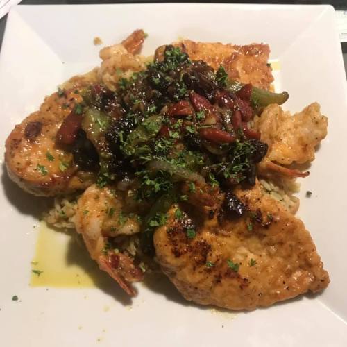 A plate of seasoned shrimp and fish topped with sautéed vegetables, served over rice and garnished with herbs.