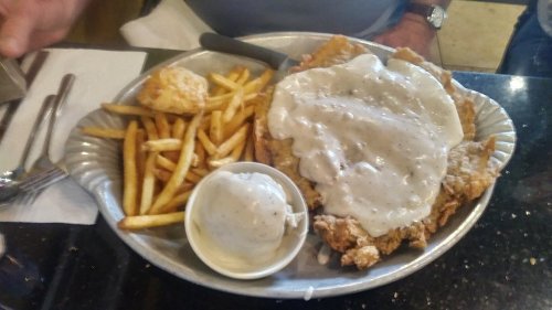 A metal platter with fried chicken, gravy, fries, and a scoop of mashed potatoes.