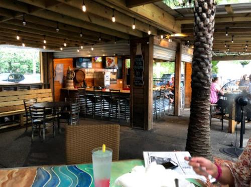 Outdoor dining area with wooden beams, string lights, and a view of a casual restaurant. A drink sits on the table.