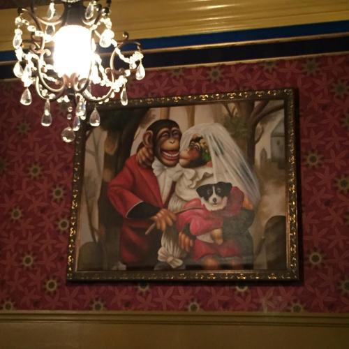A whimsical painting of a monkey couple in wedding attire, with a dog, hanging under a chandelier.