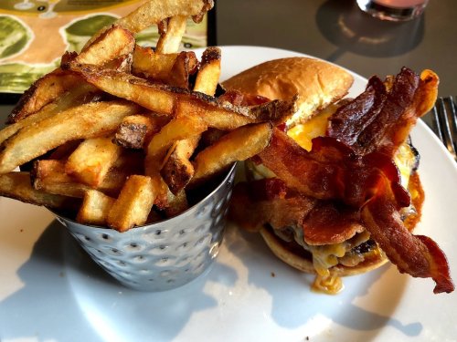 A plate featuring a bacon cheeseburger with melted cheese and a side of crispy French fries in a metal cup.