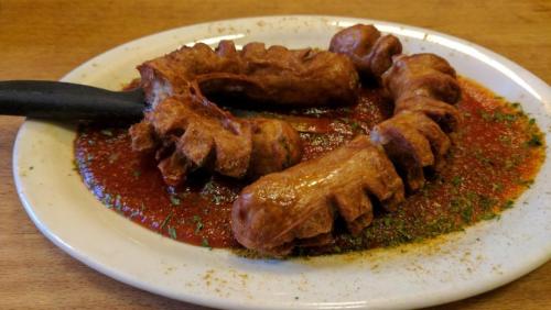 A plate of fried sausage links in a red sauce, garnished with herbs on a wooden table.