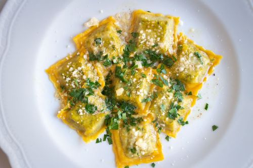 A plate of green ravioli topped with herbs and grated cheese, served on a white dish.