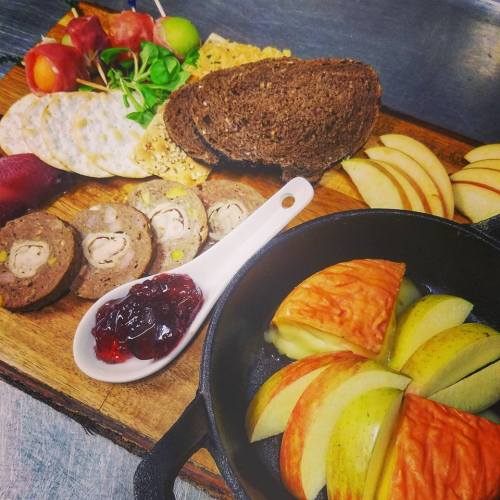 A wooden platter with assorted meats, cheeses, crackers, apples, and a small dish of jelly.