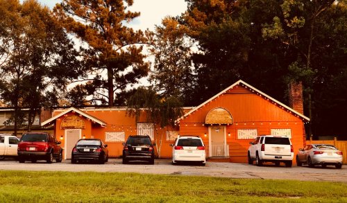 A bright orange building with decorative lights, surrounded by parked cars and trees in the background.