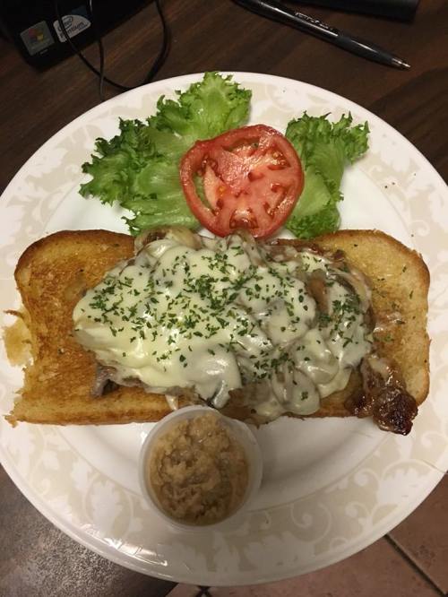 A toasted sandwich topped with melted cheese, herbs, and a side of spread, accompanied by lettuce and tomato.