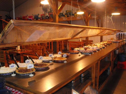 A buffet table filled with various pies and desserts under a wooden canopy in a rustic dining setting.