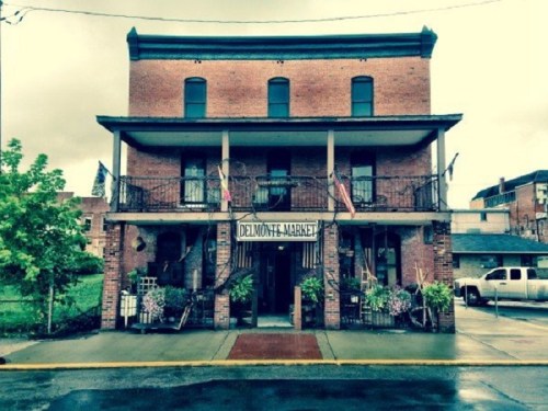 Historic brick building with a sign reading "Delmonte Market," featuring balconies and greenery in front.