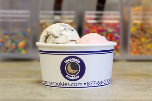 A cup of ice cream with two scoops: one cookies and cream, one pink, in front of colorful sprinkles.