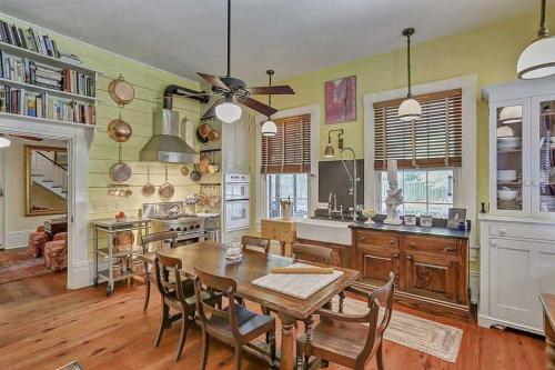A cozy kitchen with a wooden dining table, yellow walls, and modern appliances, featuring shelves of books and decorative items.