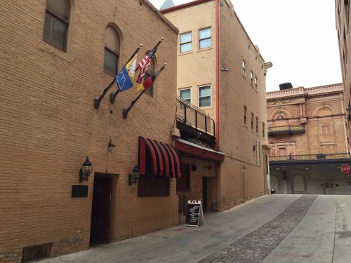 Narrow alleyway with brick buildings, flags hanging, and a restaurant entrance with a striped awning.