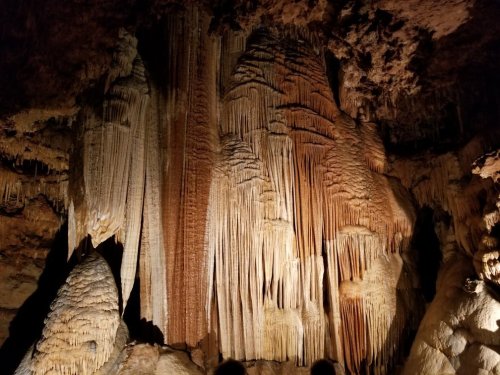 Stalactites and stalagmites in a dimly lit cave, showcasing intricate rock formations and textures.