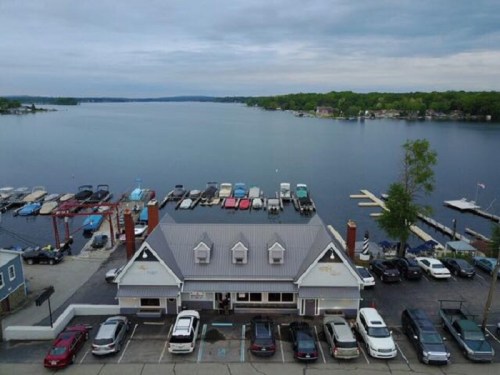 Aerial view of a marina with boats docked, a restaurant by the water, and a calm lake under a cloudy sky.