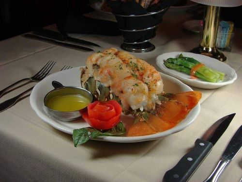 A plate of shrimp and lobster tail garnished with a rose-shaped tomato and served with a side of dipping sauce.