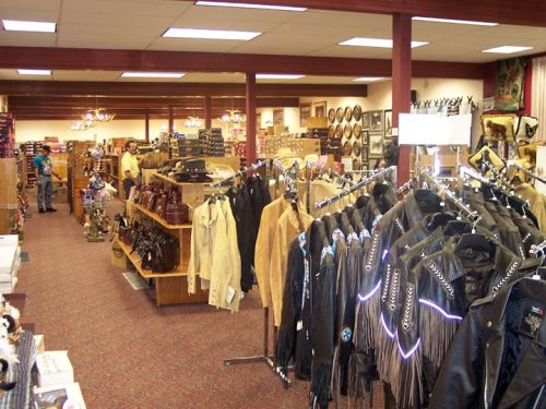 A spacious store interior filled with leather jackets and western merchandise, with shoppers browsing the aisles.