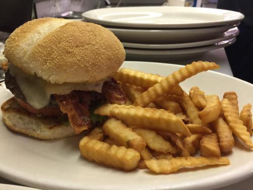 A juicy burger with cheese and bacon, served with a side of crinkle-cut fries on a white plate.
