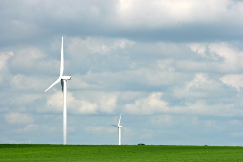 Two wind turbines stand in a green field under a cloudy sky.