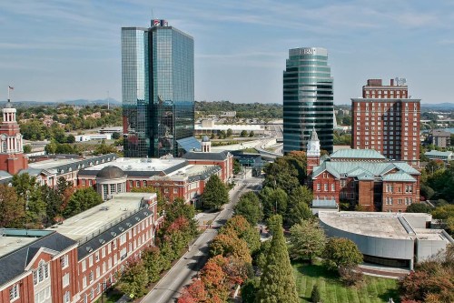 Aerial view of a cityscape featuring modern skyscrapers and historic buildings surrounded by trees in autumn colors.