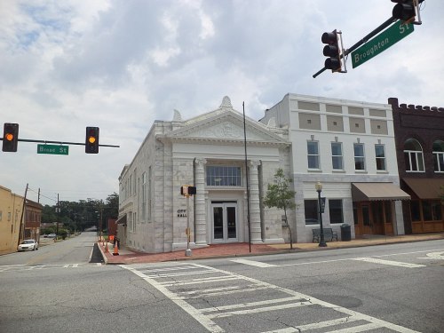 Historic city hall building at an intersection, featuring classical architecture and a cloudy sky.