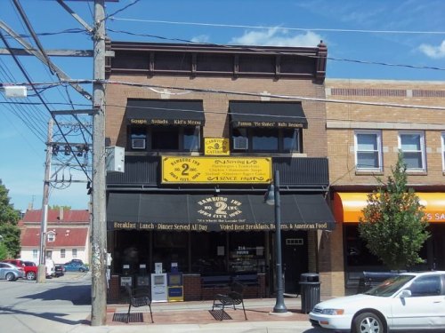 A two-story restaurant with a yellow sign, featuring outdoor seating and a menu highlighting breakfast and American food.