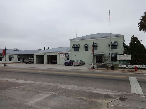 A two-story building with a flat roof, featuring striped awnings, parked cars, and a Christmas tree outside.
