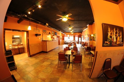 Interior of a restaurant featuring orange walls, tables, chairs, and a bar area, with a warm and inviting atmosphere.
