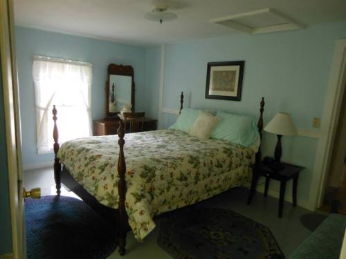 Cozy bedroom with a floral bedspread, wooden furniture, and soft blue walls, featuring a window with sheer curtains.