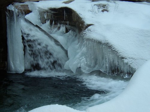A frozen waterfall cascading over icy rocks, surrounded by snow and ice formations.