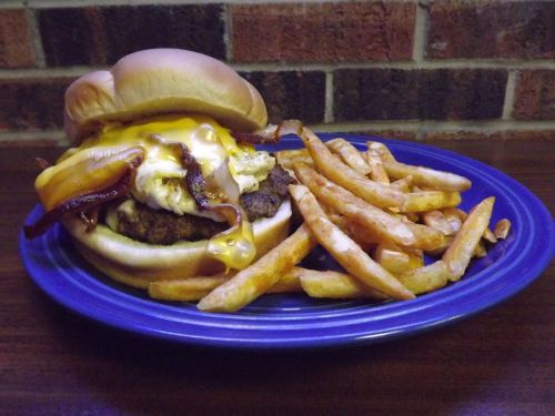 A juicy burger with cheese and bacon, served with a side of crispy French fries on a blue plate.